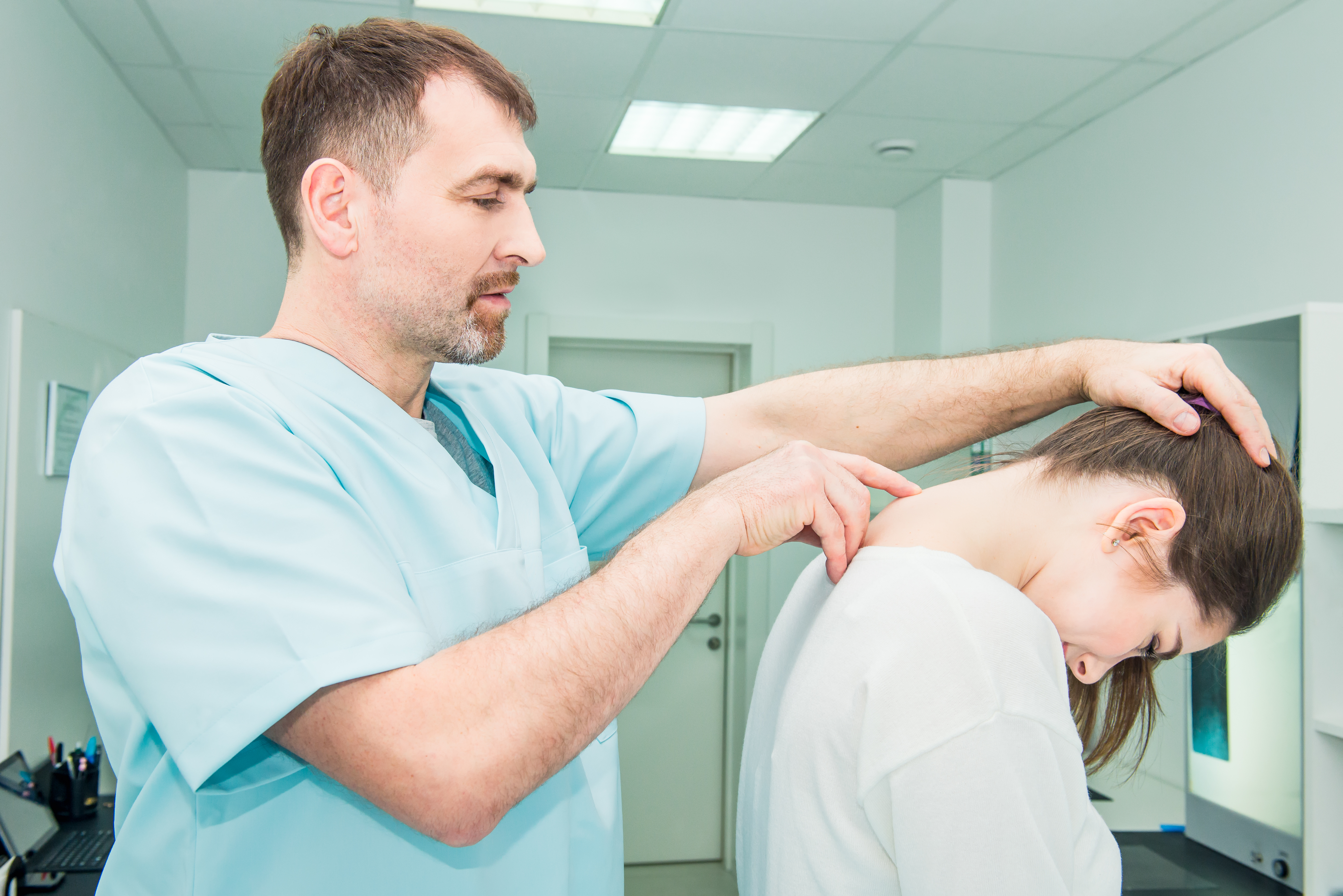 Male neurologist doctor examines cervical vertebrae of female patient spinal column in medical clinic. Neurological physical examination. Osteopathy, chiropractic, physiotherapy. Selective focus.